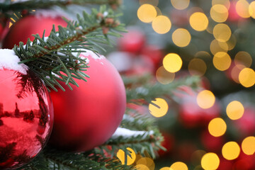 Christmas tree with red toy ball and festive illumination, golden lights on background. New Year decorations on city street covered with snow
