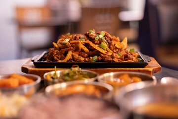 Korean pork bulgogi food and banchan side dishes on a table with artificial light at night.