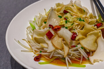 A close-up of a cold Chinese appetizer featuring thin slices of pork ear/tendon and bean sprouts tossed in a dark sauce.