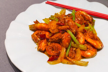 A close-up of whole shrimp stir-fried in a rich spicy sauce with sliced onions, celery, and dried chili peppers.