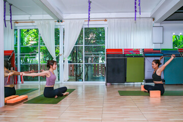 Group of women practicing seated yoga stretching with resistance bands inside a bright and modern fitness studio.