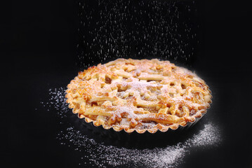 Apple pie sprinkled with powdered sugar on black background