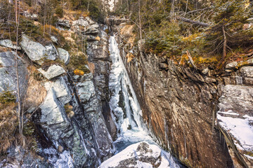 Majestic waterfall cascading through a rocky gorge with snow-kissed edges, nestled among vibrant trees during the winter season.  High Tatras National Park, Slovakia, Europe.