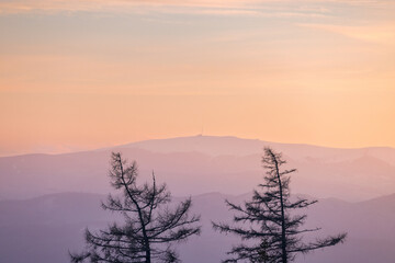 The Kralova hola peak in Low Tatras National Park, Slovakia, Europe. Silhouette of leafless trees against a backdrop of softly layered mountains and a pastel-hued sky at sunset. © Viliam
