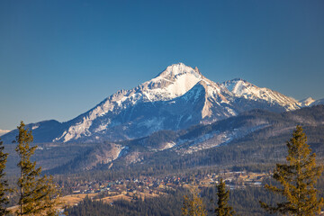 Majestic snow-capped mountain peak rising above a dense forest, a picturesque village nestled in the valley below. Zakopane town at the foot of the Tatra Mountains in Poland, Europe.