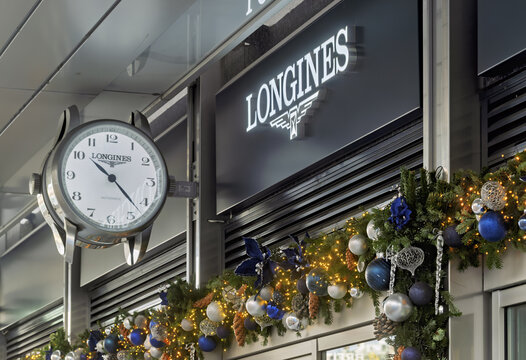 Geneva, Switzerland &ndash; December 10, 2025 : signs and logotype of Storefront of Longines featuring a large round clock with the brand name Below the sign, a festive garland decorated with silver, blue, 