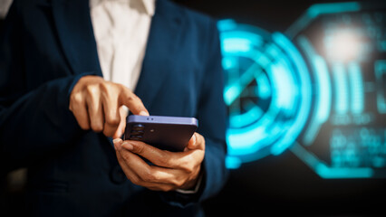 A business professional woman in a dark blue suit uses a smartphone in front of glowing digital dashboards, highlighting data analytics, technology integration, modern in futuristic workspace.