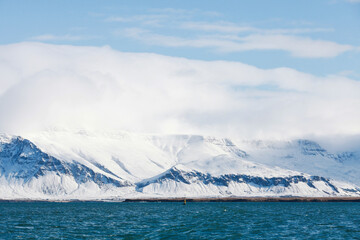 Mountains covered with snow meet a deep blue sea in a tranquil wintry landscape