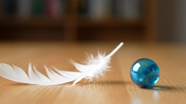 A white feather lies next to a blue orb on a wooden surface, with a blurry background