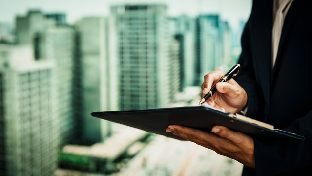 Business professional writing on clipboard with pen against an urban skyline, documentation, corporate workflow, decision-making,  modern professional responsibilities in a city business environment.