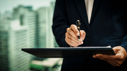 Business professional writing on clipboard with pen against an urban skyline, documentation, corporate workflow, decision-making, modern professional responsibilities in a city business environment.