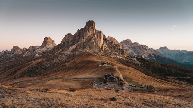 Golden sunrise over Passo Giau with Ra Gusela mountain peak, wooden lodge and winding road in Dolomites, Italy