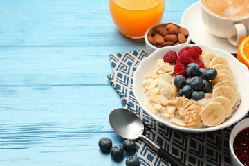 Healthy breakfast. Oatmeal with nuts, banana, berries, jam, coffee and juice on light blue wooden table, closeup. Space for text