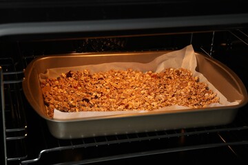 Tasty granola with dried fruits baking in oven, closeup