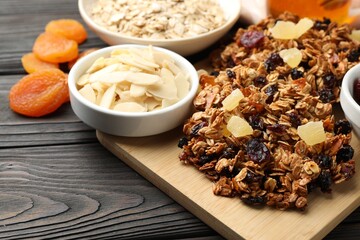 Tasty granola bars with dried fruits and nuts on black wooden table, closeup