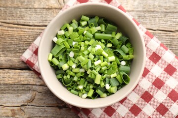 Bowl with cut green onions on wooden table, top view