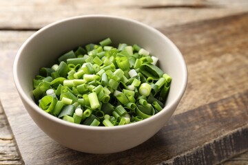 Bowl with cut green onions on wooden table, closeup