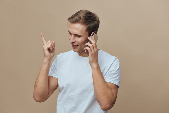 Young smiling man talking on mobile phone wearing casual white t-shirt indoors isolated on beige background concept communication technology lifestyle - Powered by Adobe