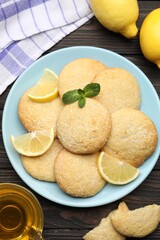 Tasty lemon cookies and fruit slices on black wooden table, flat lay