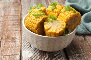 Pieces of boiled corncobs with green onion in bowl on wooden table, closeup