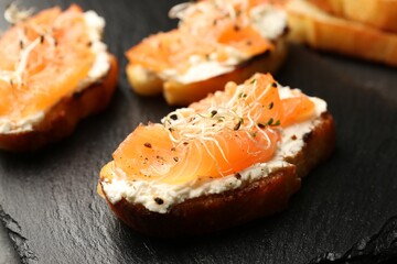 Tasty bruschettas with salmon, cream cheese and microgreens on black slate board, closeup