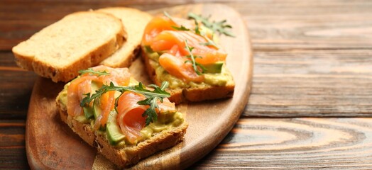 Tasty bruschettas with salmon, arugula and avocado on wooden table, closeup. Space for text