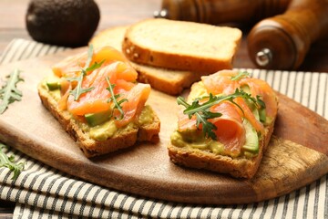 Tasty bruschettas with salmon, arugula and avocado on wooden table, closeup