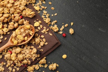 Tasty granola with dried fruits and spoon on black table, top view. Space for text
