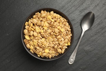 Tasty granola in bowl and spoon on black table, flat lay