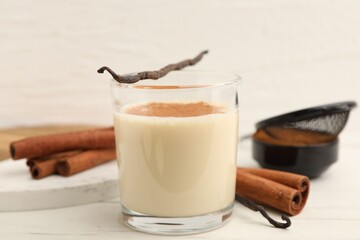 Delicious protein shake in glass, cinnamon and vanilla pods on white wooden table, closeup