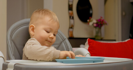 Naklejka premium Young boy sits comfortably in a chair, munching on a colorful piece of fruit. The warm kitchen setting highlights his enjoyment of this healthy snack during a quiet moment.