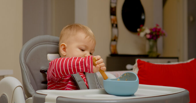 A cheerful baby boy explores the joys of self-feeding during breakfast at home. His concentration and excitement shine through as he enjoys his meal with a spoon.