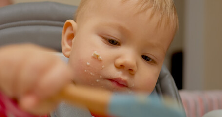 A little boy in a high chair happily eats cereal for breakfast. He explores self-feeding and demonstrates growing independence. This fun mealtime shows the joy of learning for children.