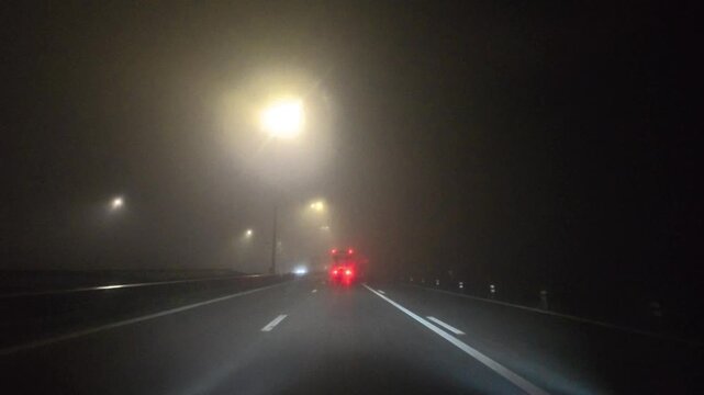dense city fog red brake lights ahead, rideshare driver navigates dim expressway, windshield wiper streaks create blurred vision,