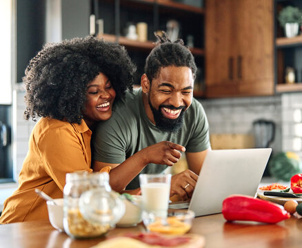 Happy young afro american couple having fun preparing food and looking for recipes online using a laptop in kitchen