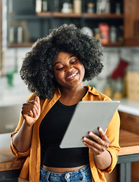 Fototapeta Happy young afro american woman having fun preparing food and looking for recipes online using a tablet in kitchen, or a young businesswoman working from home office making connections online