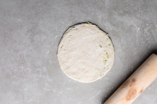 Overhead view of rolled out raw chinese scallion pancakes on a white plate, top view of homemade scallion pancakes, process of making cong you bing