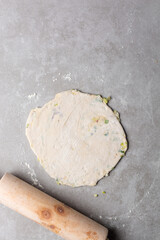 Overhead view of rolled out raw chinese scallion pancakes on a white plate, top view of homemade scallion pancakes, process of making cong you bing
