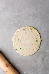 Obraz premium Overhead view of rolled out raw chinese scallion pancakes on a white plate, top view of homemade scallion pancakes, process of making cong you bing