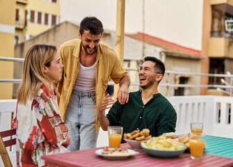 Happy young people having fun during a rooftop party during a summer holiday, sitting by the table talking, eating and drinking, love, romance, relationship, flirting and youth culture concept