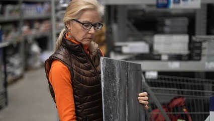 Mature woman studies a tile while shopping in a large hardware store for home renovation supplies and ideas