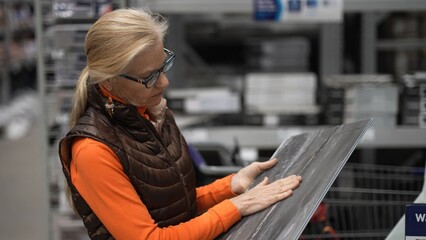 Mature woman holds a tile sample in a bright hardware store while looking for materials for home...