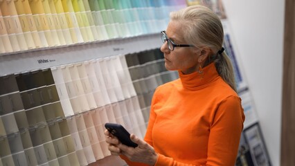 A mature woman is examining paint swatches while shopping in a hardware store for home renovation materials