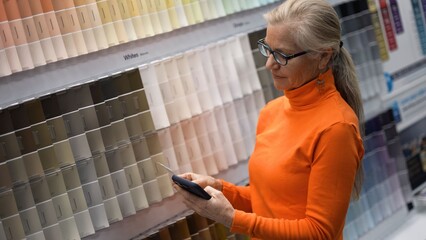 Mature woman examines paint color samples while shopping in a large hardware store for home improvement projects and renovation ideas
