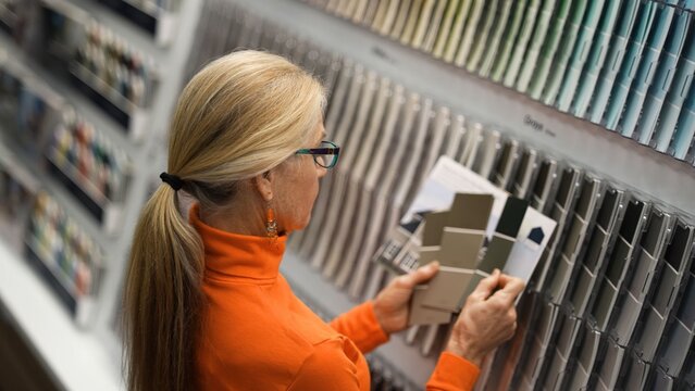 Mature woman looks at paint samples while shopping in a hardware store for home renovation needs during the day