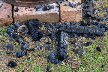 Close-up texture of campfire remnants: scattered pieces of black, charred wood (charcoal) and ash among dry grass after an outdoor camping event. Background for nature, survival, or fire safety.