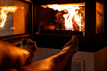 A pair of feet in front of the fireplace. A woman and man warm themselves by the fire.	