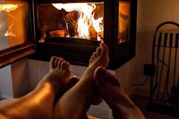 A pair of feet in front of the fireplace. A woman and man warm themselves by the fire.	