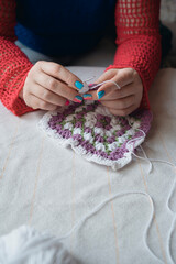 female hands crocheting colorful square napkin of multicolor yarn
