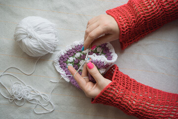 hands of woman crocheting colorful square napkin of multicolor yarn
